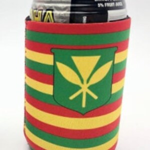May include: A colorful beverage can koozie with a Hawaiian design. The koozie features horizontal stripes in red, yellow, and green, with a green shield emblem containing a yellow symbol. The can inside is partially visible, showing a black and silver top.