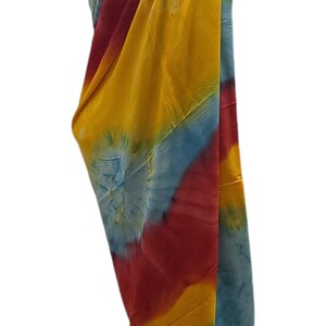 May include: A colorful tie-dye sarong with blue, yellow, and red hues. The sarong is draped over a mannequin and is ready to be worn.