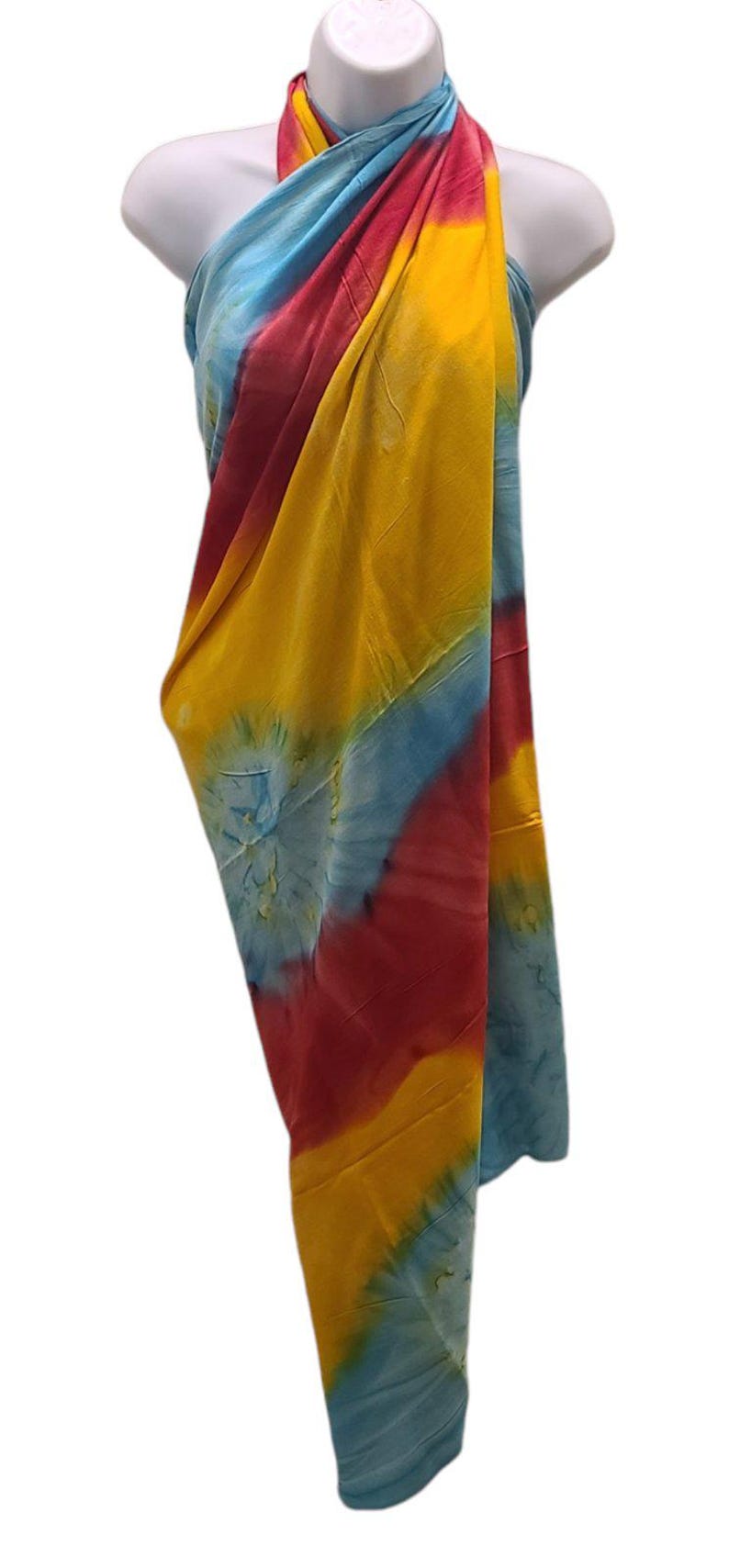 May include: A colorful tie-dye sarong with blue, yellow, and red hues. The sarong is draped over a mannequin and is ready to be worn.