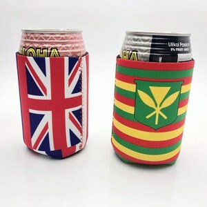 May include: Two beverage can coolers. One features the Union Jack flag in red, white, and blue. The other has a green shield with a yellow design, and red, yellow, and green horizontal stripes. Both are made of a neoprene-like material.