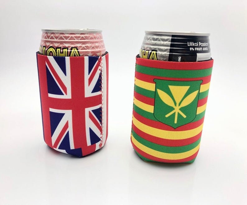 May include: Two beverage can coolers. One features the Union Jack flag in red, white, and blue. The other has a green shield with a yellow design, and red, yellow, and green horizontal stripes. Both are made of a neoprene-like material.