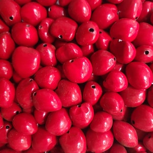 May include: A close-up image of a pile of bright red heart-shaped beads. The beads are smooth and glossy, and they are all the same size.