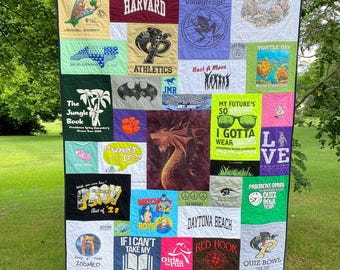 May include: A colorful quilt made from a variety of t-shirts. The quilt features a variety of designs, including a dragon, a turtle, a peace sign, and the words "What if?" and "I Gotta Wear".