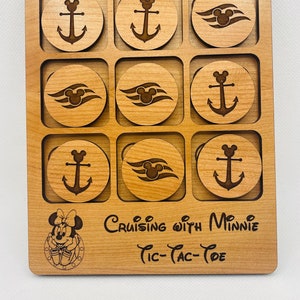 May include: Wooden tic-tac-toe game with anchor and Mickey Mouse head designs. The game board has a Minnie Mouse graphic and the text "Cruising with Minnie Tic-Tac-Toe". The game pieces are circular and fit into square recesses.