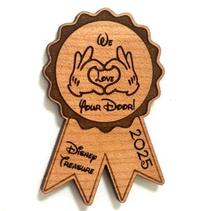 May include: Wooden Disney Treasure ornament with a brown ribbon and the text "We Love Your Door!" and "2025". The ornament features a heart shape made with two hands.
