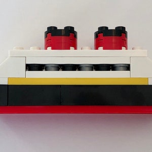 May include: A white, red, black, and yellow Lego ship model. The ship has two red smokestacks with black tops, a yellow stripe, and a black hull.