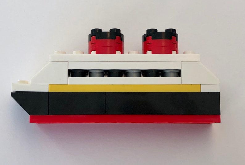 May include: A white, red, black, and yellow Lego ship model. The ship has two red smokestacks with black tops, a yellow stripe, and a black hull.