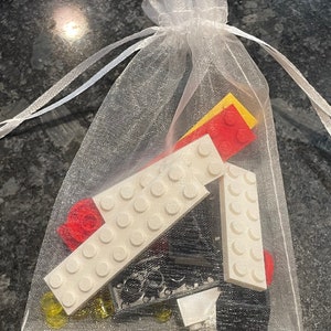 May include: A white mesh bag filled with various LEGO bricks, including white, red, yellow, and black pieces.