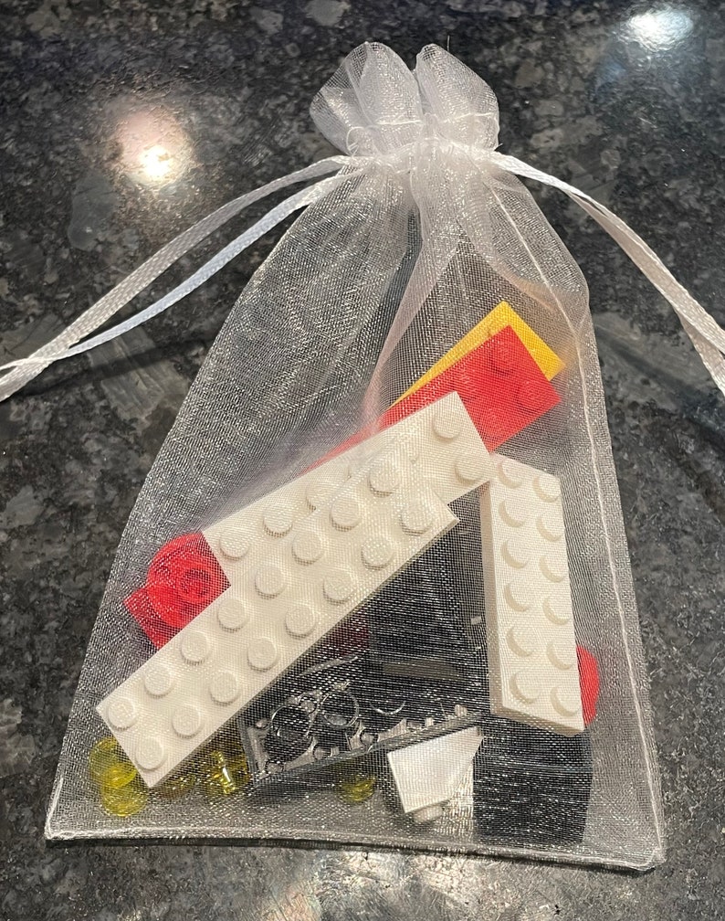 May include: A white mesh bag filled with various LEGO bricks, including white, red, yellow, and black pieces.