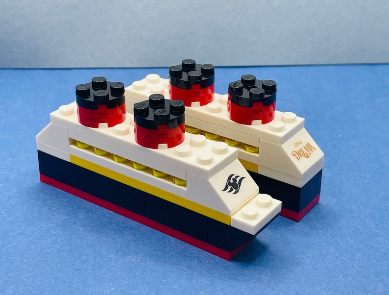 May include: A white and black Lego model of a cruise ship with red and black smokestacks. The ship has the words "Disney Dream" printed on the side.