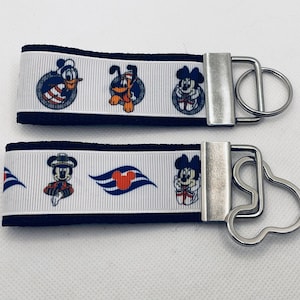 May include: Two black and white keychains with a white background and colorful Disney characters. The top keychain features Mickey Mouse, Pluto, and Donald Duck. The bottom keychain features Mickey Mouse as a captain, the Disney cruise line logo, and Mickey Mouse.
