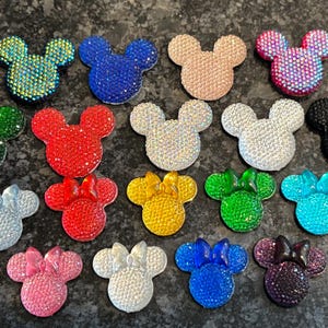 May include: Assortment of 16 colorful rhinestone Mickey Mouse head embellishments. The embellishments are in various colors, including red, blue, green, pink, yellow, and black.