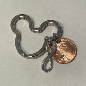 May include: Silver Mickey Mouse shaped keychain with an infinity symbol charm and a 2021 US penny attached.