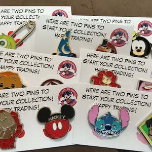 May include: Six white cards with the text "Here are two pins to start your collection! Happy trading!" and various Disney character pins attached. The pins include Mickey Mouse, Stitch, Ariel, a character from The Lion King, a character from Monsters Inc., and a character from Lilo & Stitch.