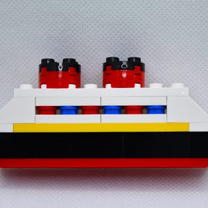 May include: A white, red, black, and blue Lego ship with four portholes and two red smokestacks.