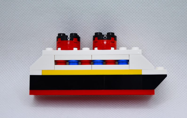 May include: A white, red, black, and blue Lego ship with four portholes and two red smokestacks.