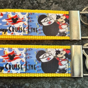 May include: Two Disney Cruise Line keychains. The keychains have a blue background with Mickey Mouse and Donald Duck graphics. The keychains have a yellow border and a silver metal clasp.