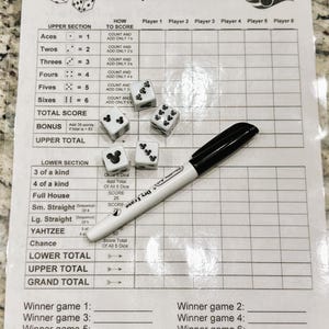 May include: A Mickey Yahtzee at Sea game set with a score sheet, dice, and a black marker. The dice are white with black pips and Mickey Mouse silhouettes. The score sheet has sections for scoring and player names.