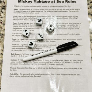 May include: A sheet of paper with the rules for "Mickey Yahtzee at Sea" is shown, along with five dice and a black dry-erase marker. The dice have Mickey Mouse icons and numbers.