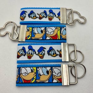 May include: Four blue and white keychains with a silver key ring. Each keychain features a different cartoon image of Donald Duck.