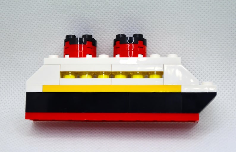 May include: A white, red, black, and yellow Lego model of a cruise ship with two red smokestacks.