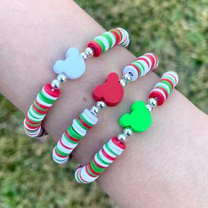 May include: Three bracelets with red, white, and green striped beads. Each bracelet has a different colored Mickey Mouse head charm: white, red, and green.
