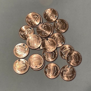 May include: A pile of copper-colored US pennies with a hole punched through the center of each coin. The coins are arranged in a random pattern. The coins are all dated 1982.
