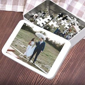 May include: A white metal puzzle box with a lid open, revealing a partially assembled puzzle. The puzzle image shows a wedding couple under an umbrella. The date "February 2, 2019" is printed on the puzzle.
