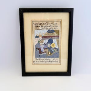 May include: A framed miniature painting featuring two figures on horseback engaged in a scene near a tent, surrounded by Arabic calligraphy on a cream-colored background. The artwork is enclosed in a simple, thin black rectangular frame.