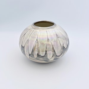 May include: A round ceramic vase with a wide opening and a short neck. The surface features a glossy, iridescent white glaze that drips downward over a dark, charcoal-colored base, creating a layered, fluid effect with a metallic sheen.