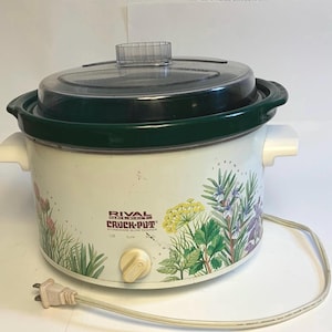 May include: A white Rival Select Crock-Pot stoneware slow cooker with a dark green rim and a clear glass lid. The exterior features a botanical print of herbs and the text "Rival Select Crock-Pot" with a control knob for Off, Low, and High settings.