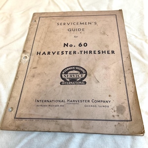 May include: A vintage Servicemen's Guide for No. 60 Harvester-Thresher. The cover is tan with black text and a logo for McCormick-Deering Service International. The guide is from the International Harvester Company, located in Chicago, Illinois.