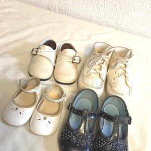 Puede incluir: Una colección de seis pares de zapatos de bebé vintage en varios estilos. Los zapatos incluyen zapatos con hebilla de cuero blanco, zapatillas con cordones crema, Mary Janes blancas con detalles florales y Mary Janes de charol negro.