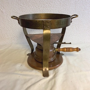 Peut inclure: Fondue antique en cuivre et en laiton avec une poignée en bois et une base ronde en cuivre. La casserole est posée sur un support à trois pieds.