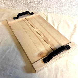 May include: A rectangular wooden serving tray with a natural finish. The tray features two black metal handles, one at each end. The wood grain is visible, and the tray is constructed with a simple, rustic design.
