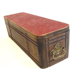 Peut inclure: Une boîte rectangulaire en bois avec une finition brun foncé et une surface supérieure rouge texturée. La boîte présente une poignée de tirage décorative en métal de couleur laiton sur le panneau avant, ornée de lignes rainurées.