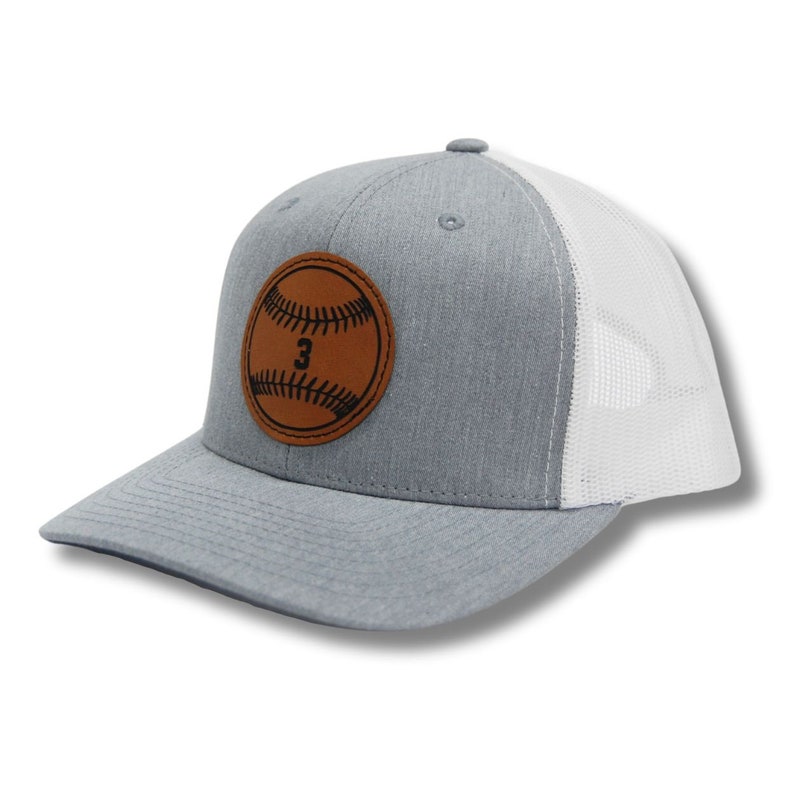 May include: A gray and white trucker hat with a brown leather patch featuring a baseball with the number 3 on it.