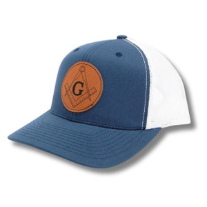 May include: A navy blue and white trucker hat with a brown leather patch featuring a compass, square, and the letter "G".