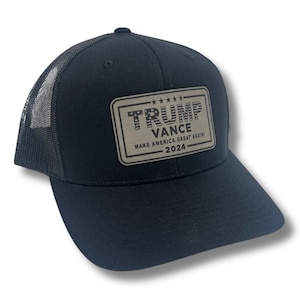 May include: Black trucker hat with a brown patch that says "TRUMP VANCE MAKE AMERICA GREAT AGAIN! 2024" with a small American flag in the upper left corner of the patch.