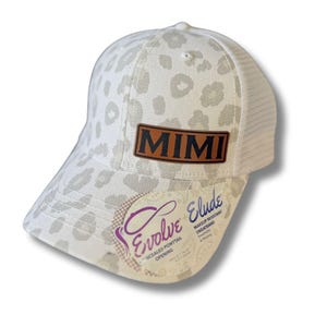 May include: A white and gray leopard print baseball cap with a mesh back. The cap features a brown leather patch with the name "MIMI" and a tag with the text "Evolve" and "Elude".