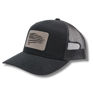 May include: A black trucker hat with a distressed American flag patch on the front. The hat has a mesh back.