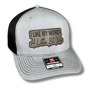 May include: A gray and black trucker hat with a black patch that reads "I LIKE MY WOMEN A LITTLE BIT OLDER". The hat is adjustable and has a Richardson logo on the back.