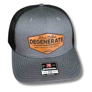 May include: Gray trucker hat with a black mesh back. The hat features a brown leather patch with the words "Blue Collar DEGENERATE" and "Dirty Hands Still Broke" printed on it. The hat is adjustable.