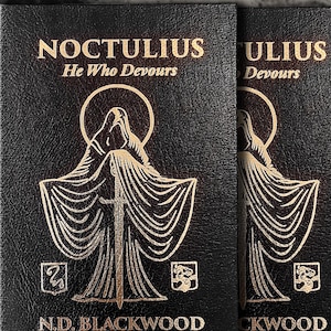 Puede incluir: Dos libros negros con letras e ilustraciones doradas. El título "NOCTULIUS" y el autor "N.D. BLACKWOOD" son visibles. La portada presenta una figura encapuchada con una espada. También está presente el texto "He Who Devours" y "Become a Living God".