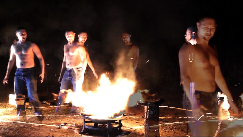 Puede incluir: Cuatro hombres sin camisa se paran alrededor de una fogata en un entorno oscuro. Los hombres llevan pantalones vaqueros y miran el fuego. El fuego es grande y brillante, con llamas que alcanzan lo alto en el aire.
