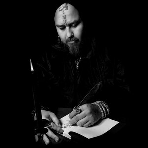 Puede incluir: Una persona con un tatuaje en la frente est&aacute; escribiendo con una pluma estilogr&aacute;fica en un papel. Una vela negra est&aacute; en el fondo.