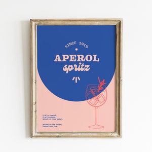 May include: A framed poster with a blue and pink background. The poster features a stylized illustration of a glass of Aperol Spritz with the text "SINCE 1919 APEROL SPRITZ" and the ingredients for the cocktail.