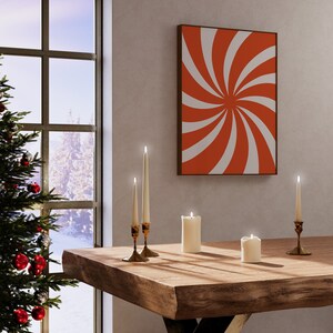 Op de afbeelding: Een houten tafel met vier witte kaarsen en twee gouden kandelaars. De kaarsen zijn aangestoken en de tafel staat voor een raam met een kerstboom en een rood-wit abstract schilderij aan de muur.