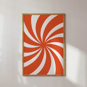 Op de afbeelding: Een ingelijst drukwerk met een draaiend oranje en wit patroon. Het patroon lijkt op een spiraal of een molen.