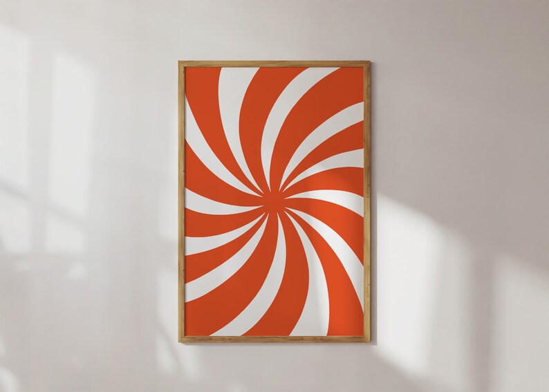 Op de afbeelding: Een ingelijst drukwerk met een draaiend oranje en wit patroon. Het patroon lijkt op een spiraal of een molen.